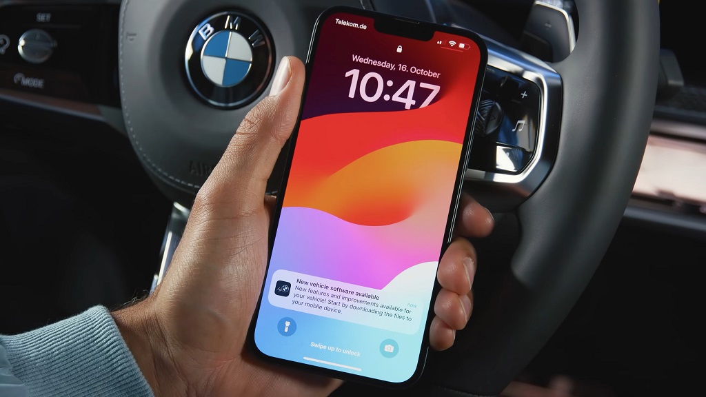 iPhone displaying a BMW vehicle software update notification while held in front of a BMW steering wheel