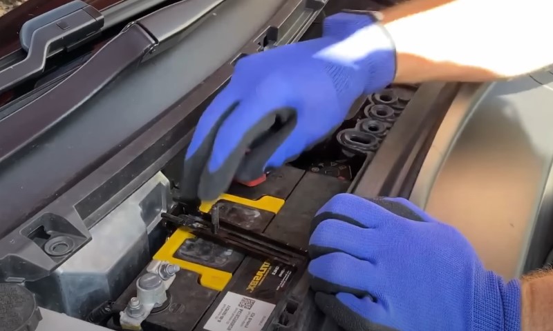 A person wearing blue gloves is inspecting and working on a car battery in a garage setting